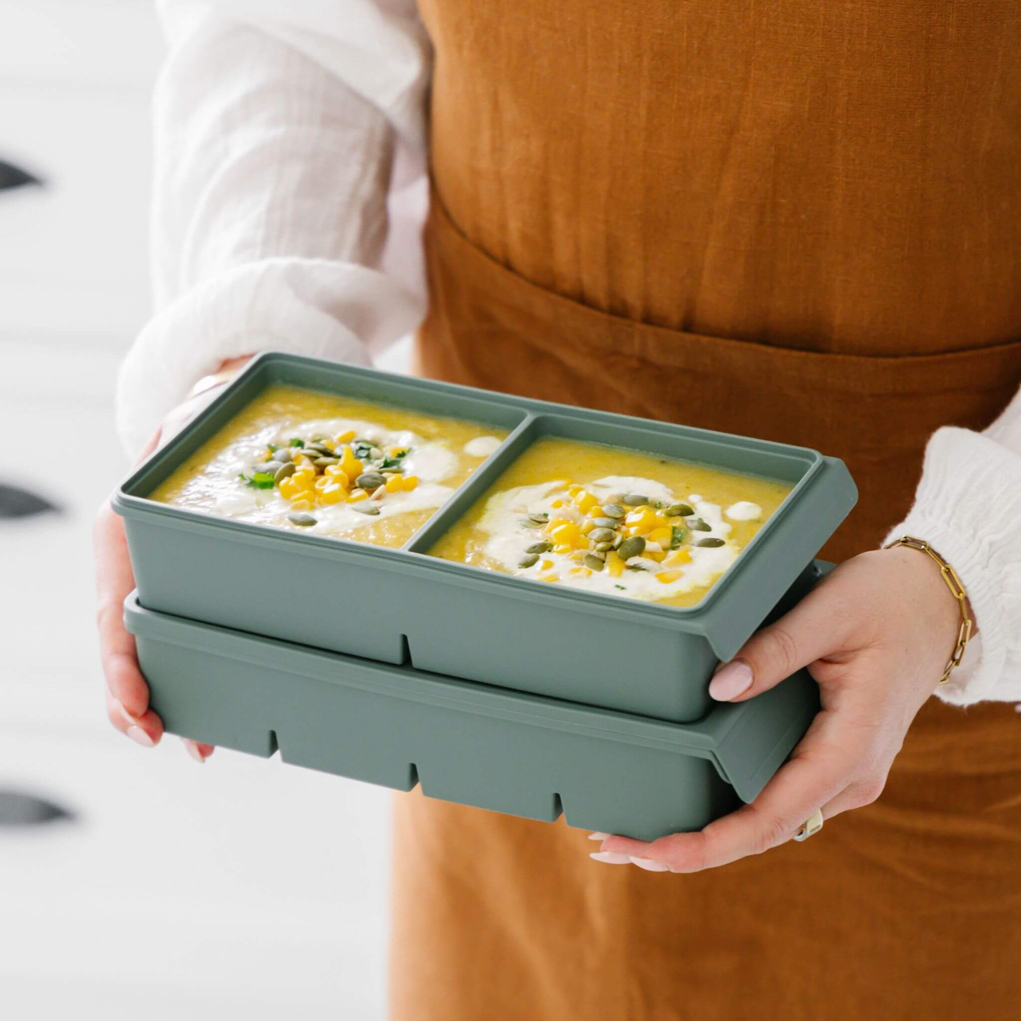 Person holding two stacked Silicone Freezer Moulds filled with portioned soup, showing the stackable design and 2 Portion 500ml tray capacity.
