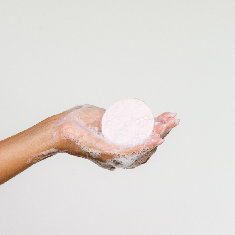 a bubbly round pink shampoo bar held in hand