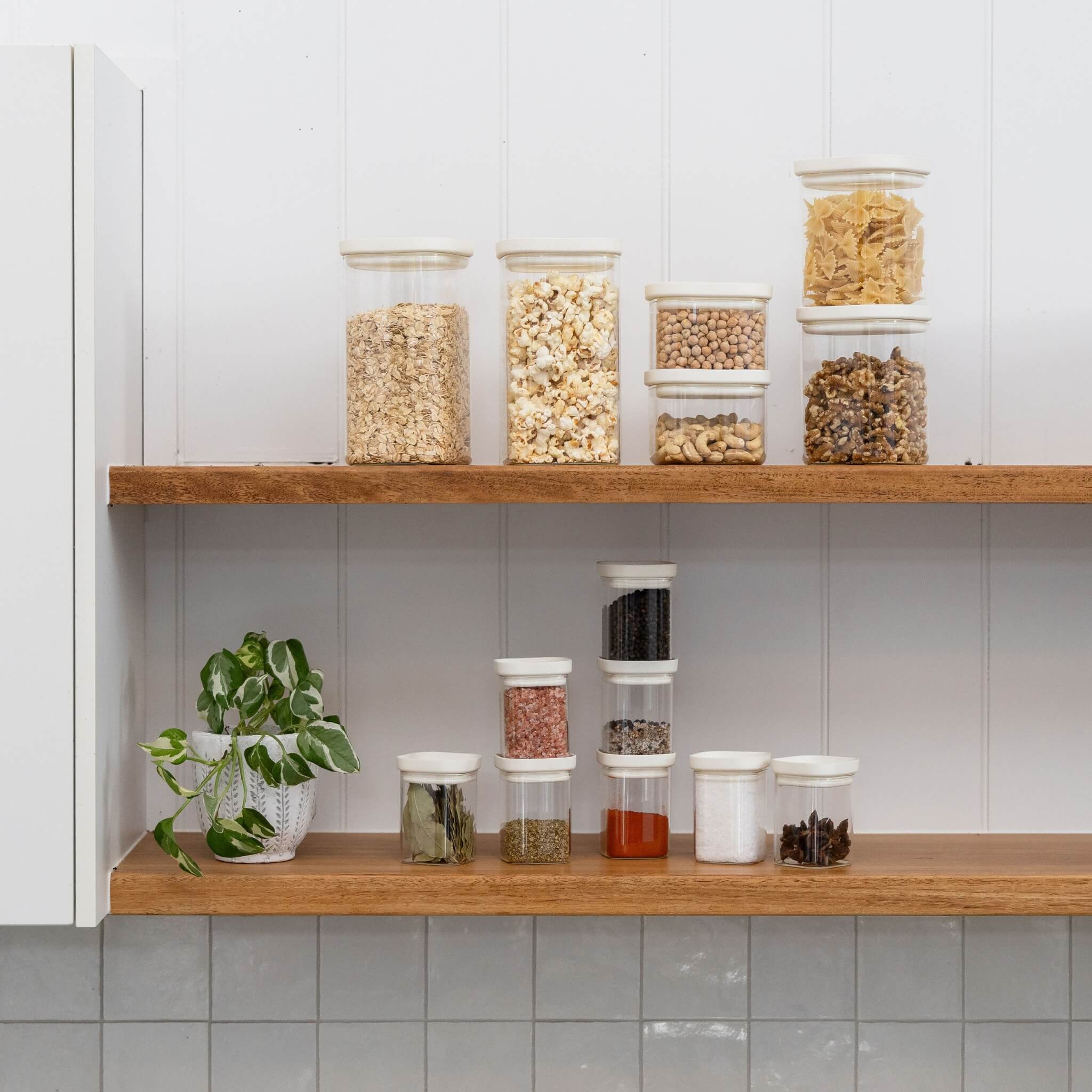 A shelf with jars on them in different sizes. They contain foods like grain, pasta, nuts, seeds and condiments